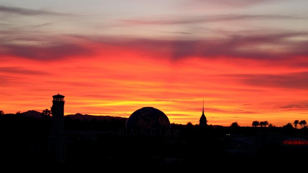A vibrant sunset over Universal Studios, with the park's iconic globe and attractions silhouetted against the evening sky, symbolizing the transition from day to night.